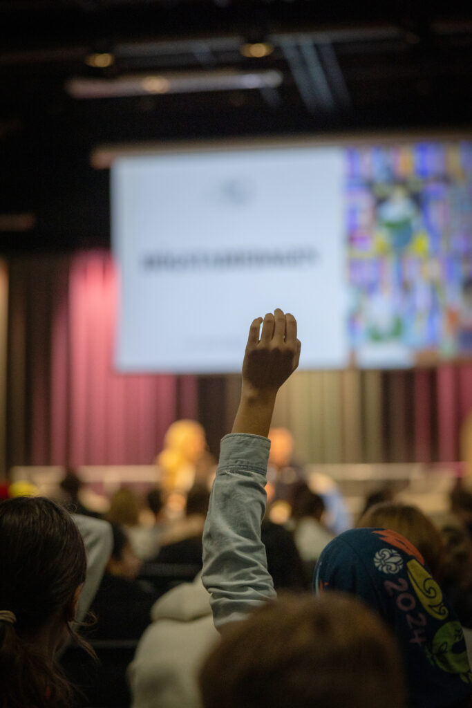 Person räcker upp handen under presentation med projektorskärm i bakgrunden