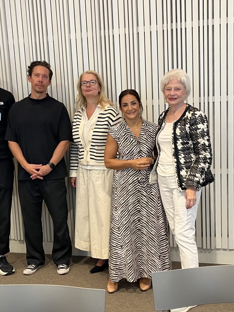 Gruppfoto med fyra personer i svartvitt och randigt framför en ribbad vägg i konferenslokal.