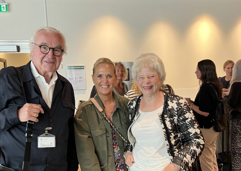 Tre personer poserar tillsammans vid mingelevent, man i svart kostym till vänster, två kvinnor i mitten och höger.